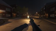 First-person view down a lamp-lit street at night with a rifle raised. An opponent stands lit up in the road near traffic cones.